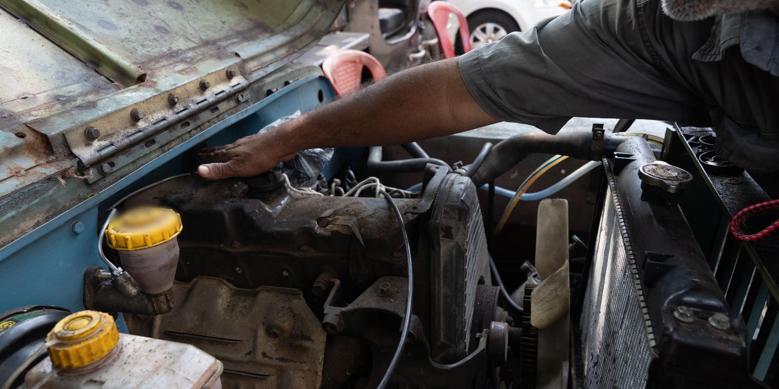 Mão apoiada sobre o motor de um carro, ao lado do reservatório de fluido de freio e do radiador